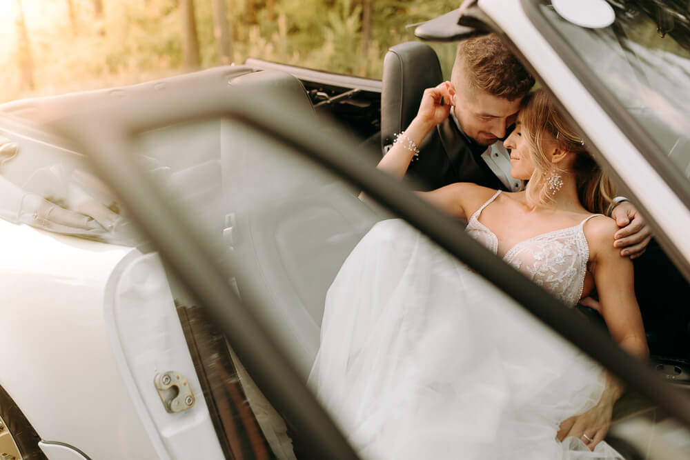 Młoda para pozuje podczas sesji ślubnej w samochodzie na tle zachodu słońca.