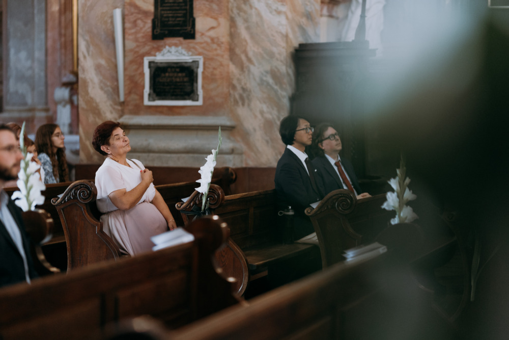 Goście weselni siedzą w ławkach kościoła podczas ceremonii ślubnej. 