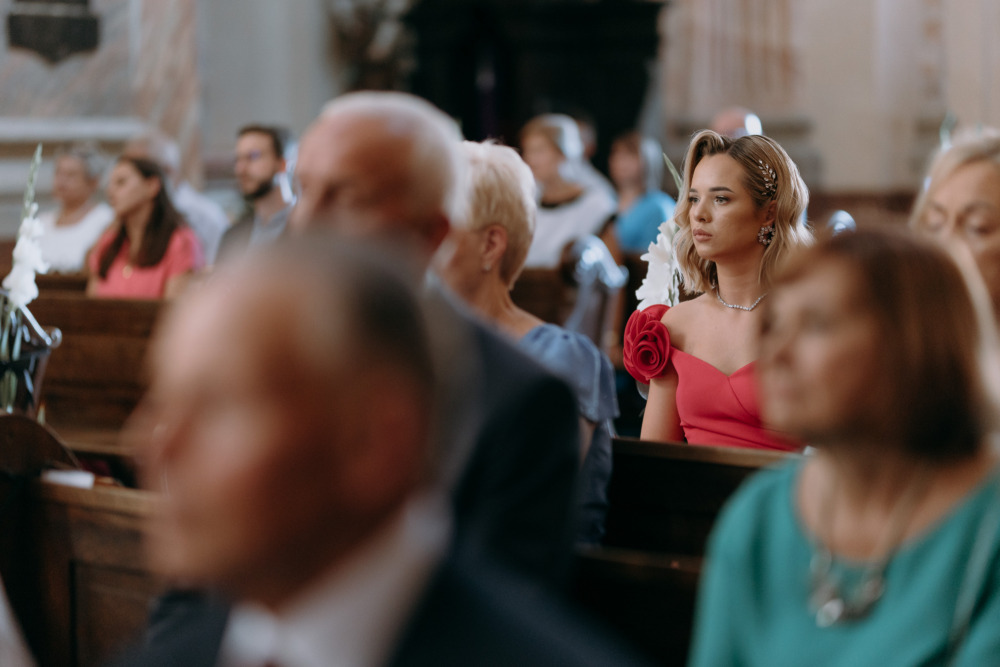Elegancka kobieta w kościele, gość weselny w różowej sukience z ozdobą z róż.