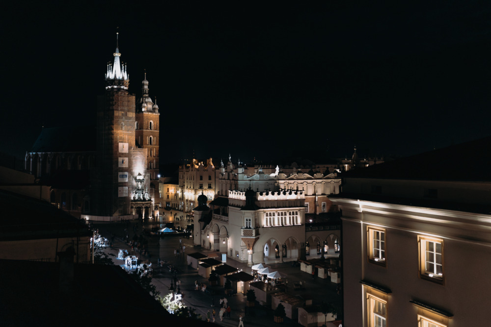 Nocny widok na Rynek Główny w Krakowie z oświetlonymi Sukiennicami i Kościołem Mariackim.