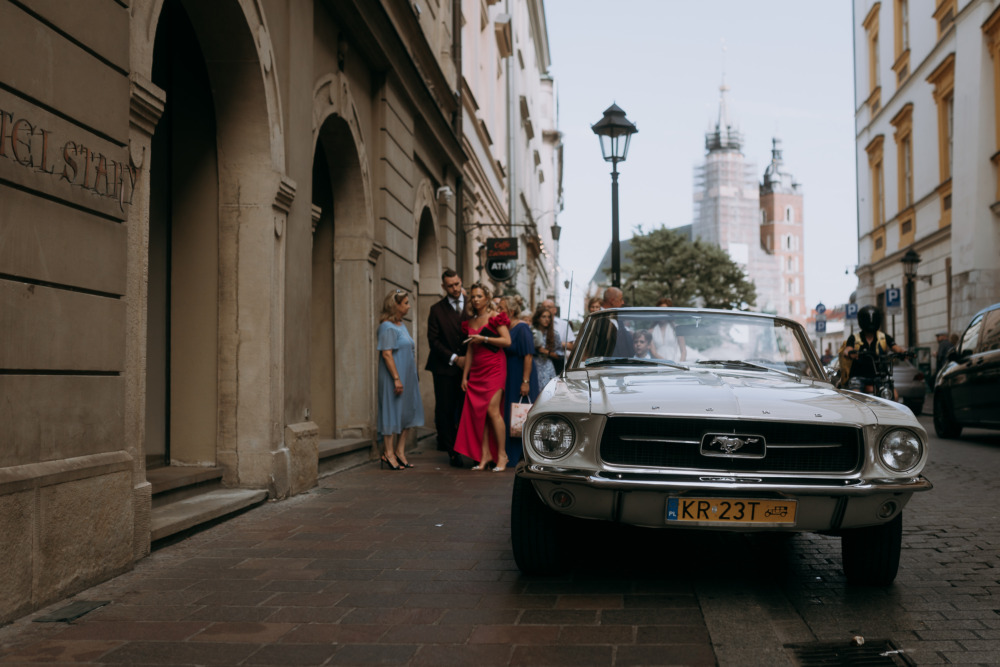 Elegancki Mustang i goście weselni na ulicy w Krakowie.