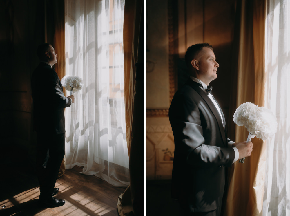 Elegancki pan młody trzyma bukiet kwiatów, patrząc przez okno.