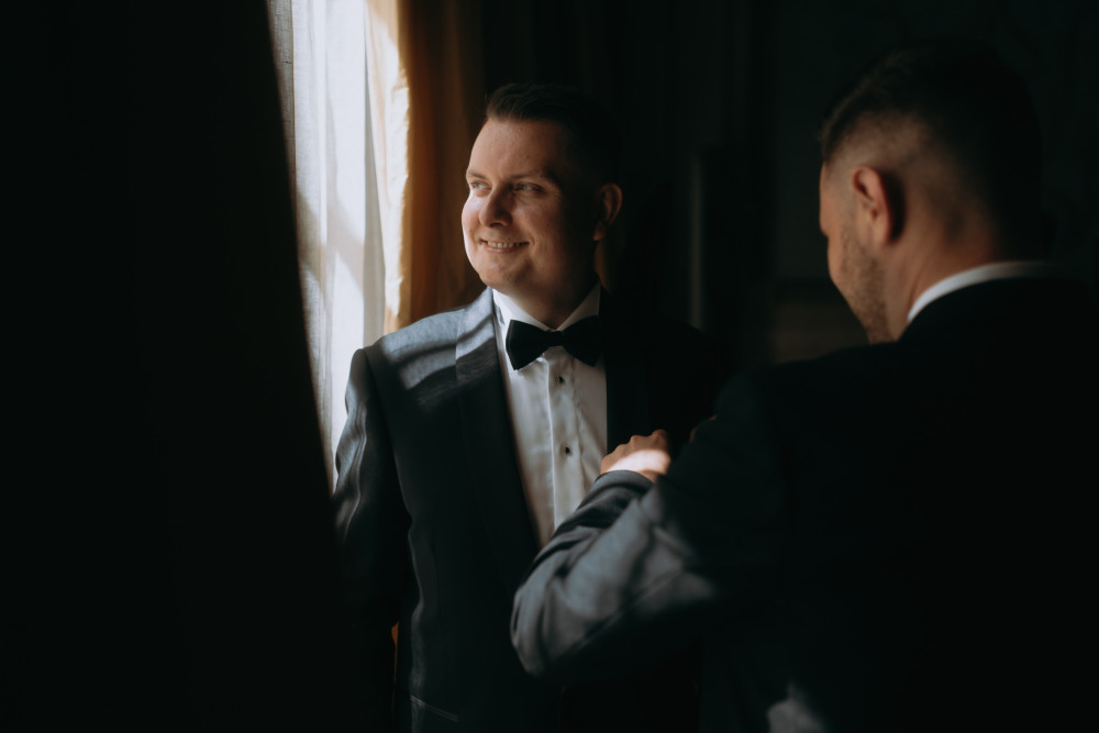Uśmiechnięty pan młody w smokingu, przygotowania do ślubu w eleganckim wnętrzu.