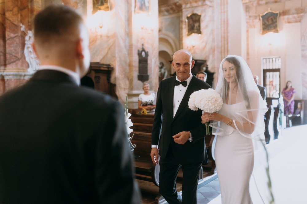 Panna młoda idzie do ołtarza z tatą. Ceremonia ślubna w kościele.