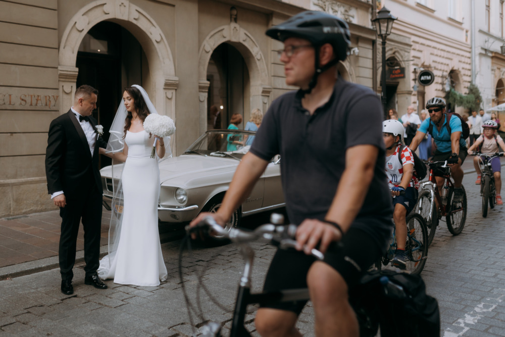Para młoda przed hotelem w Krakowie i przejeżdżający rowerzyści. Nietypowe ujęcie reportażowe.