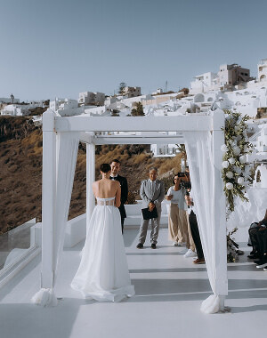 Para młoda podczas ceremonii ślubnej na Santorini, białe budynki w tle.